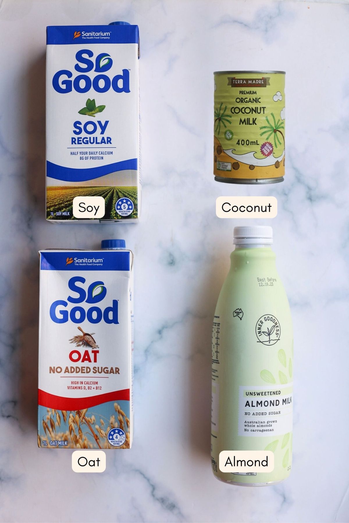 Cartons of different types of plant-based milk on a marble bench top.