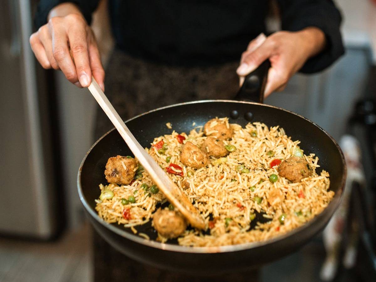A woman holding a frying pan with rice and meatballs