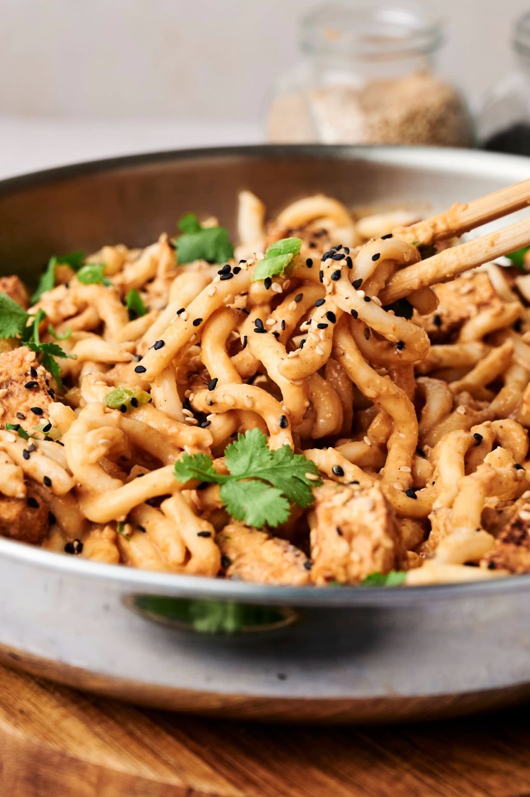 Creamy noodles topped with black sesame seeds and leafy greens.