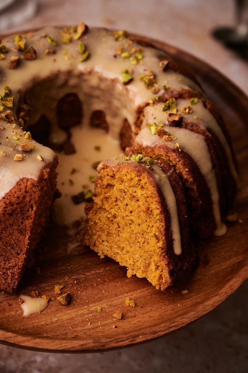 Sliced pumpkin bundt cake with orange crumb and maple glaze, on a wooden board.
