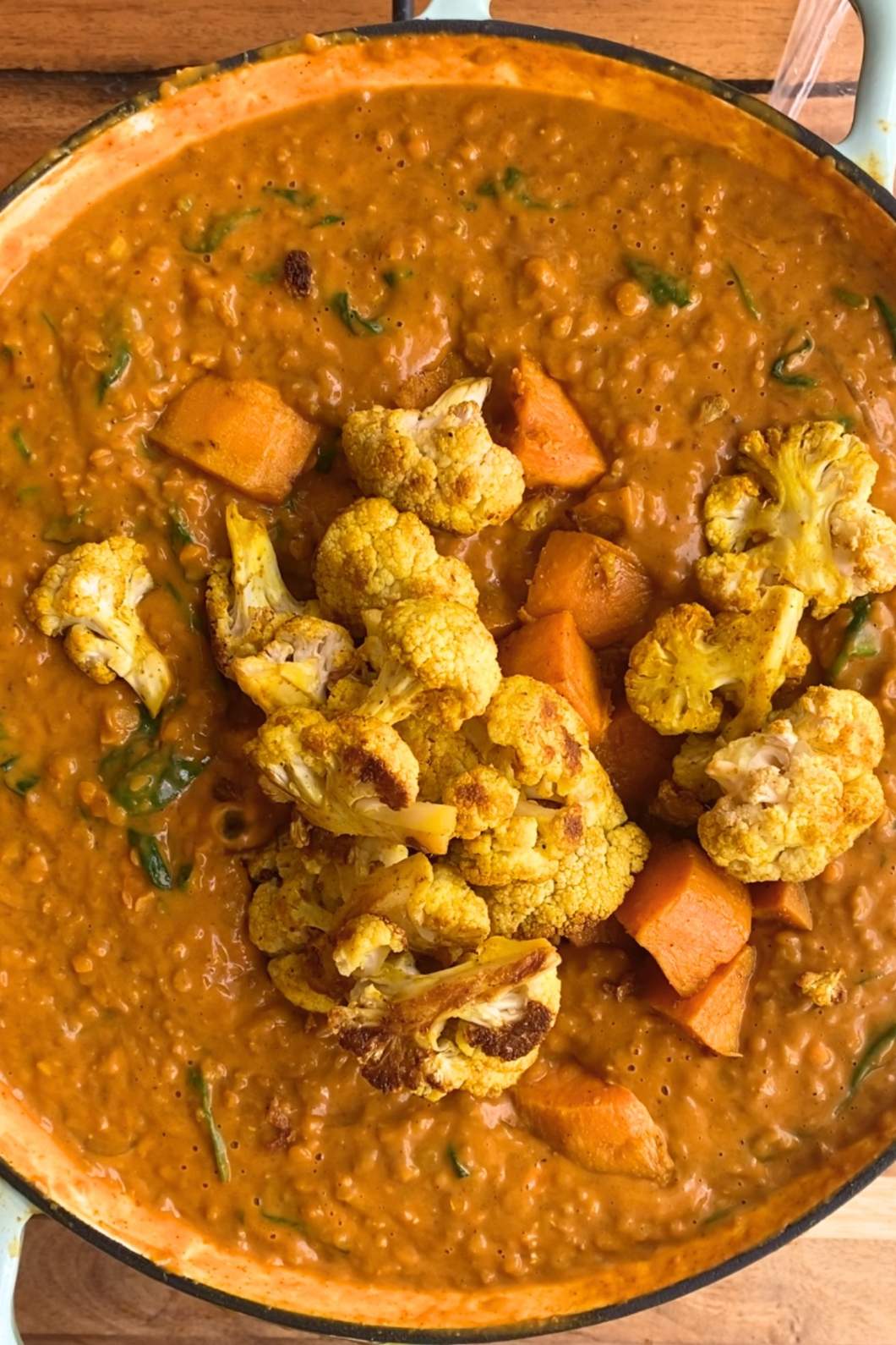 Rich, creamy lentil soup in a blue pot, topped with roasted cauliflower and chunks of sweet potato.