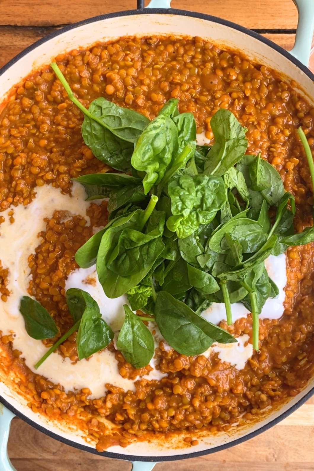 A pot of red lentil curry with a dollop of coconut milk and a handful of fresh spinach leaves on top.