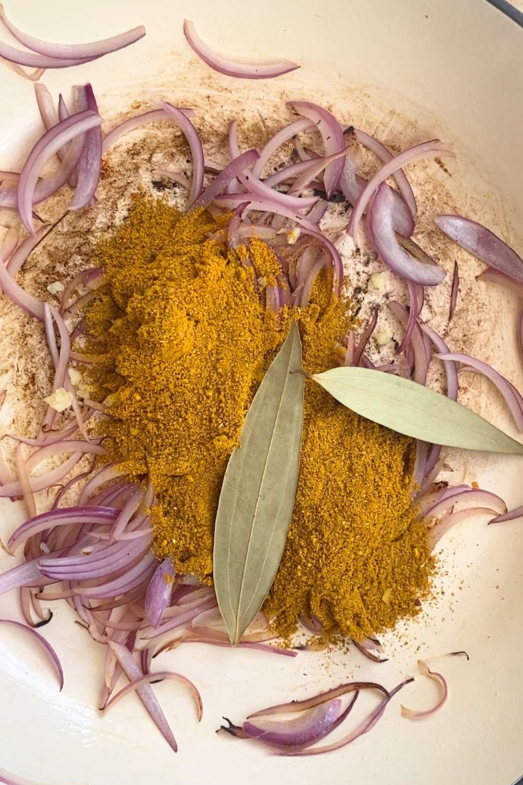 Sliced red onions, turmeric powder, and bay leaves in a pot.
