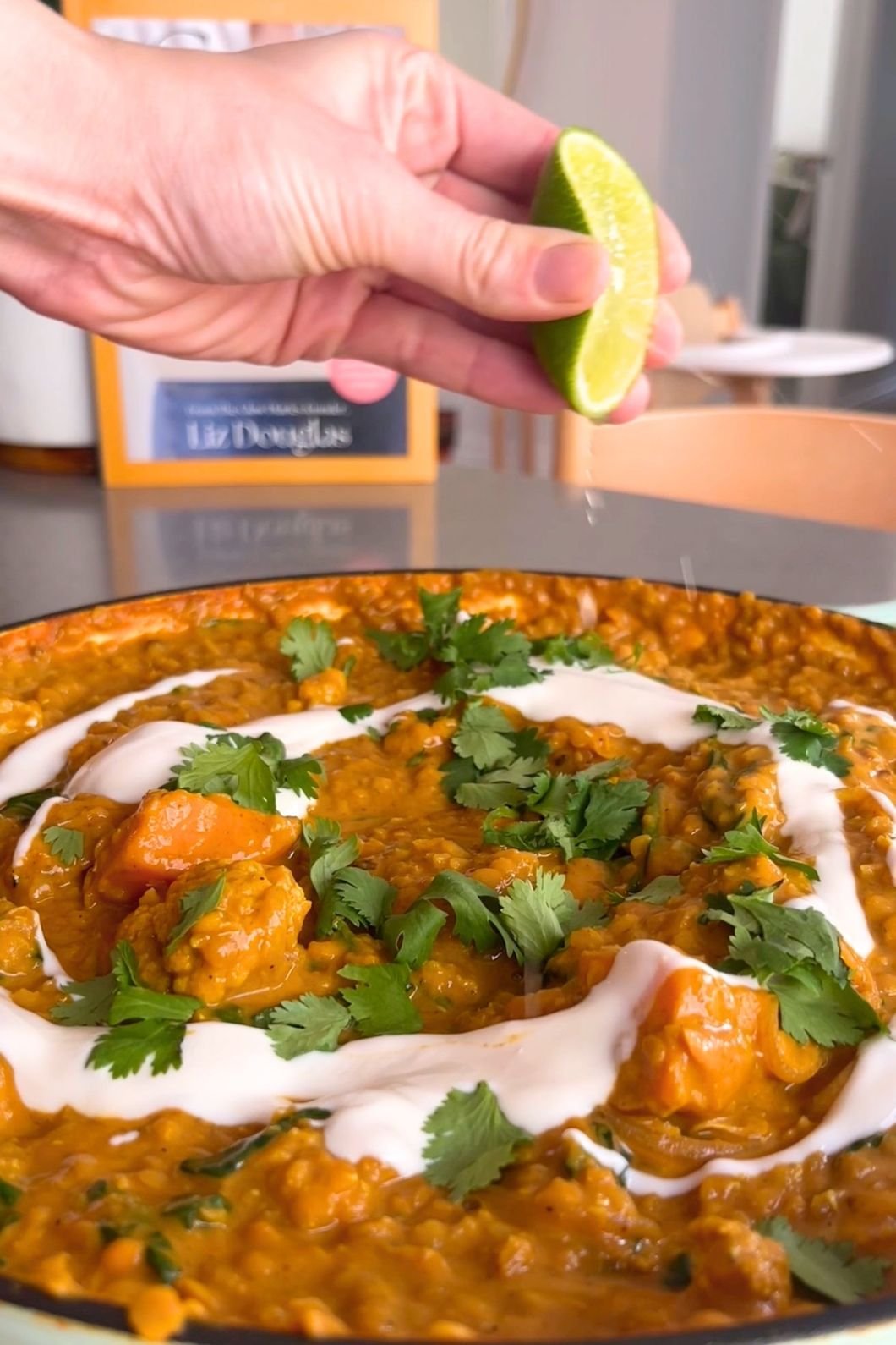 Close-up of a hand squeezing lime over a dish of creamy lentil curry, garnished with fresh cilantro and yogurt swirls.