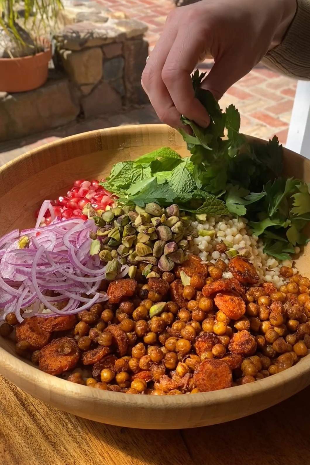 A hand places fresh herbs into a large salad bowl filled with veggies.