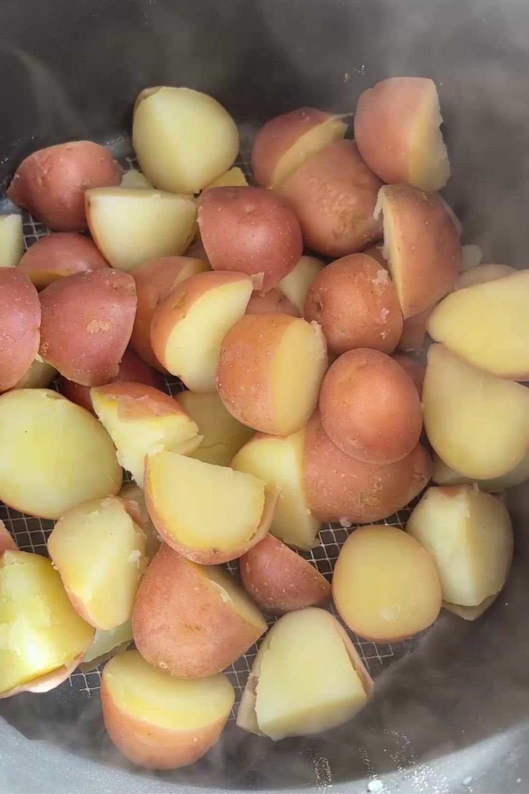 Steamed potato halves with skins visible in a colander, releasing steam.