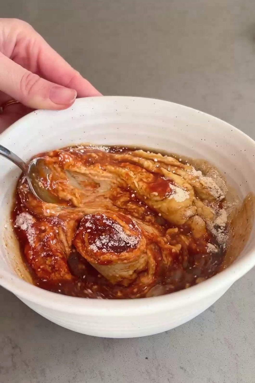A spoon lifts thick orange dressing from a white mixing bowl.
