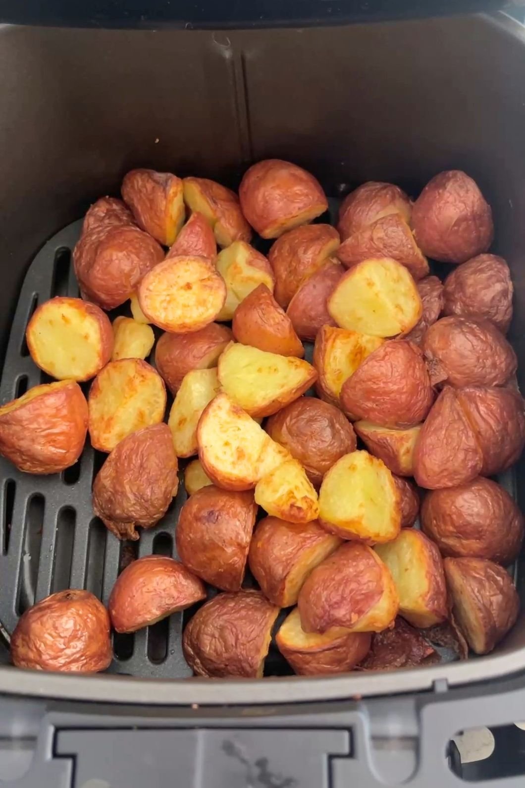 Crispy halved potatoes with golden edges resting in an air fryer basket.