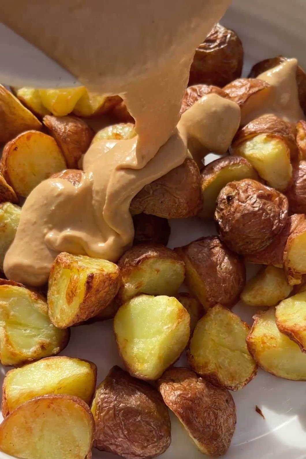 Creamy dressing being poured over roasted potatoes in a white bowl.