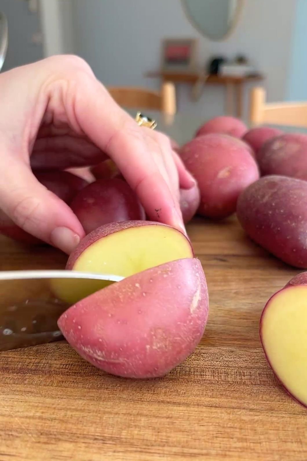 Hand slicing red-skinned baby potatoes into halves on a wooden board.