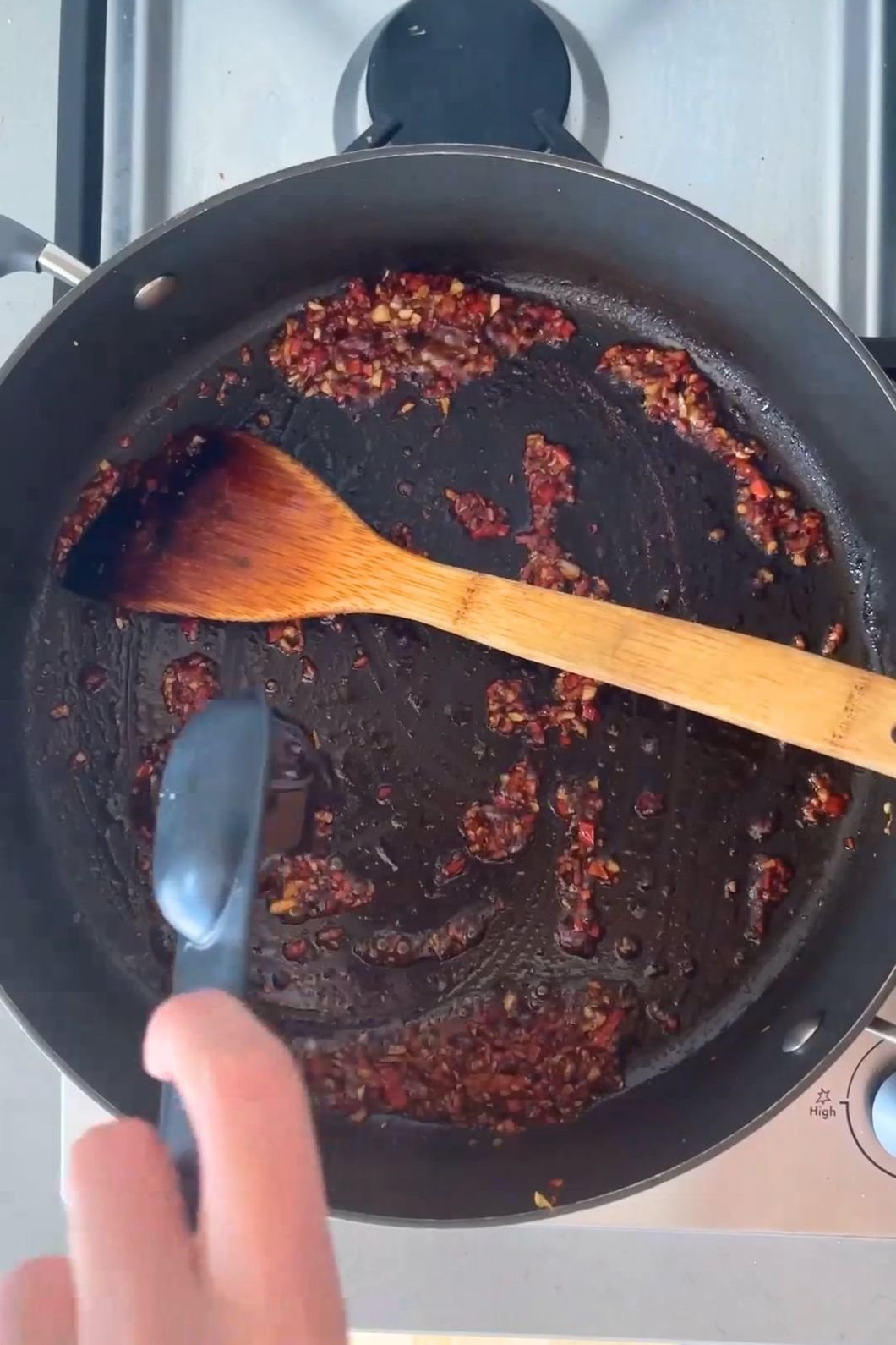 Garlic and chili mixture is being sautéed in a black pan with a wooden spoon.