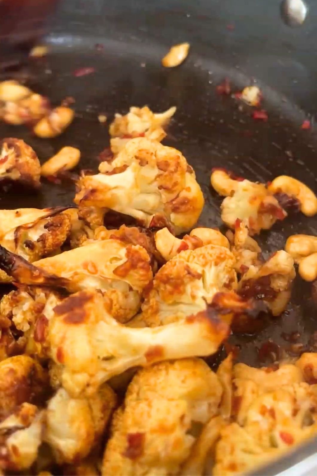 Roasted cauliflower and cashews coated in a glossy sauce in a black pan.