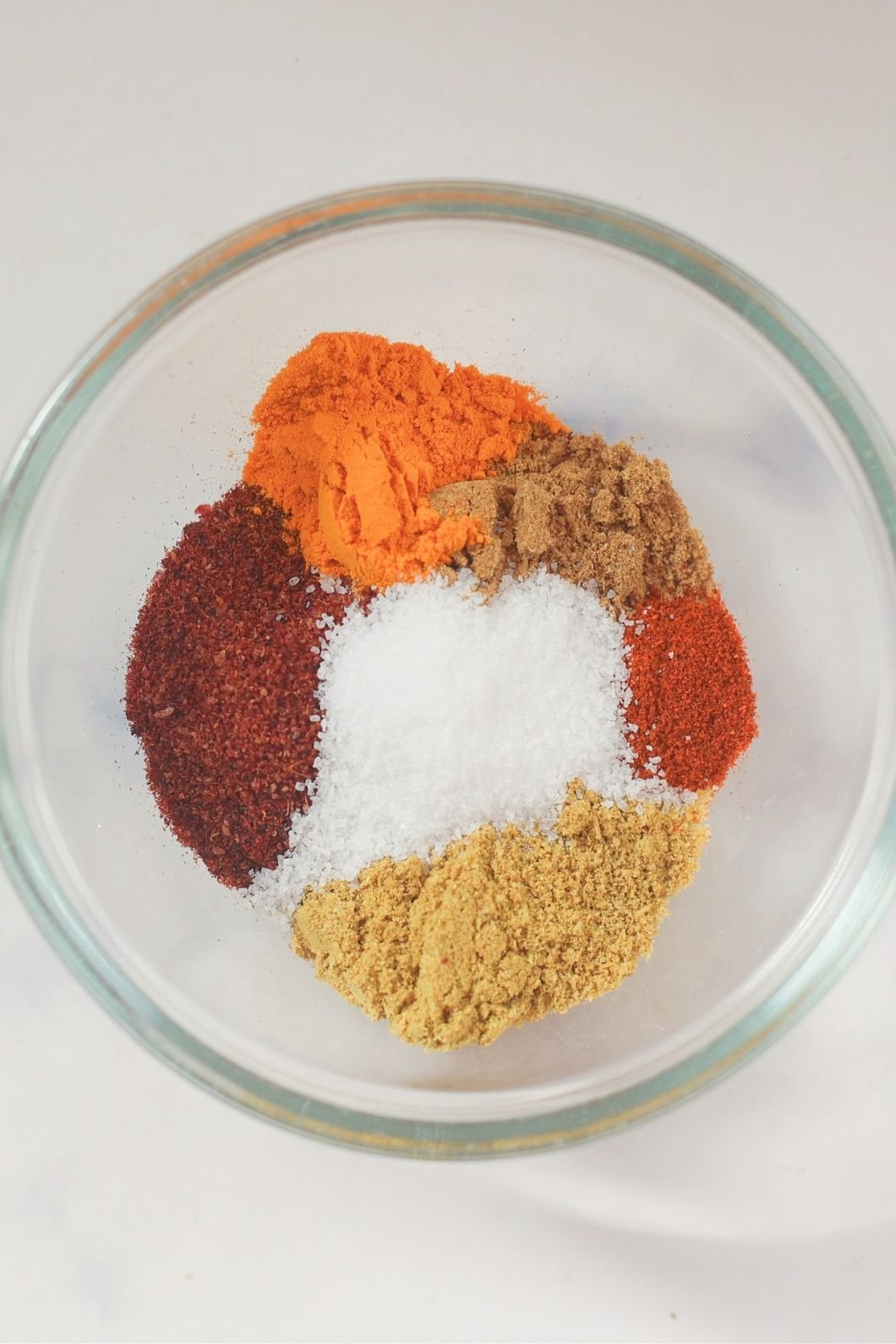 A clear glass bowl contains colorful spices arranged in sections.