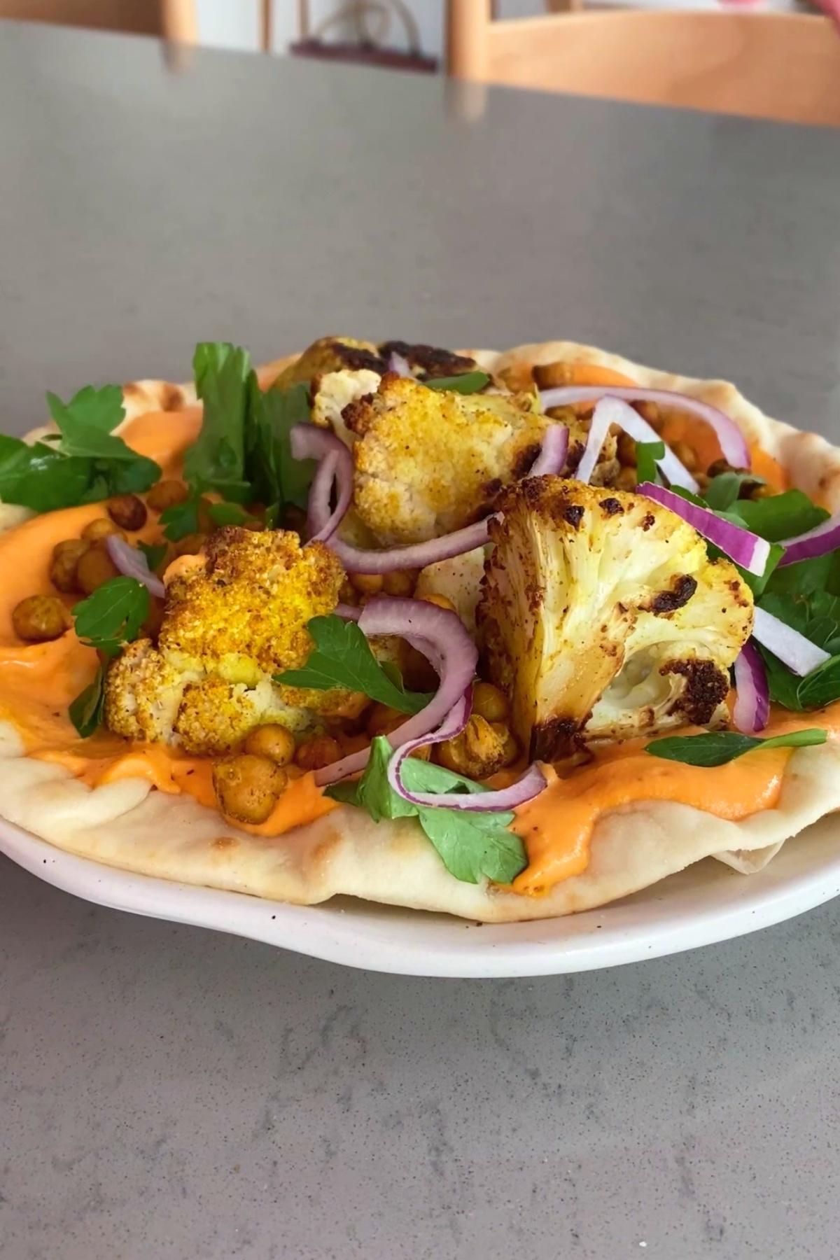 Flatbread topped with roasted cauliflower, chickpeas, red onion, and parsley over a layer of orange sauce.