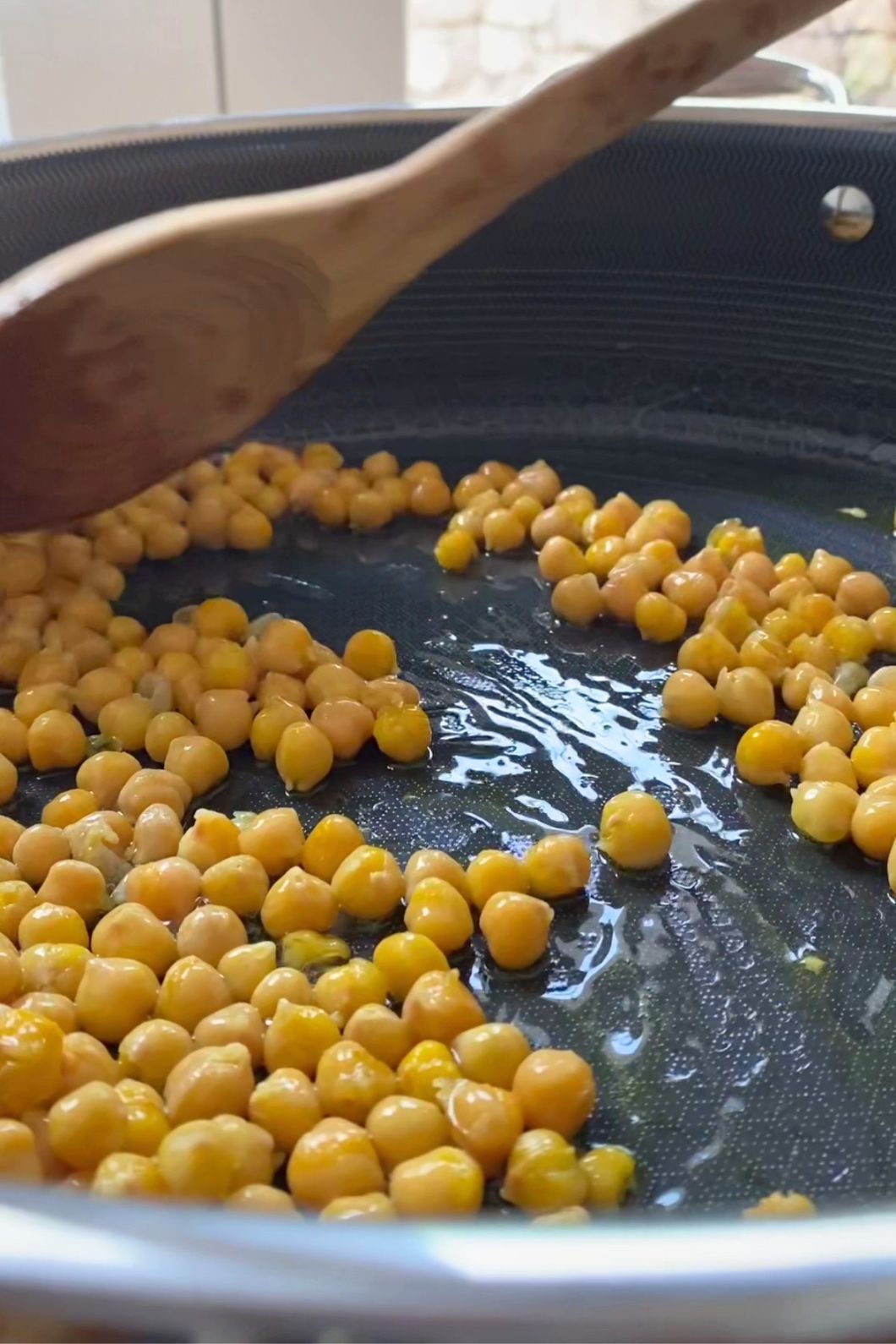 Chickpeas being sautéed in a pan with a wooden spoon.