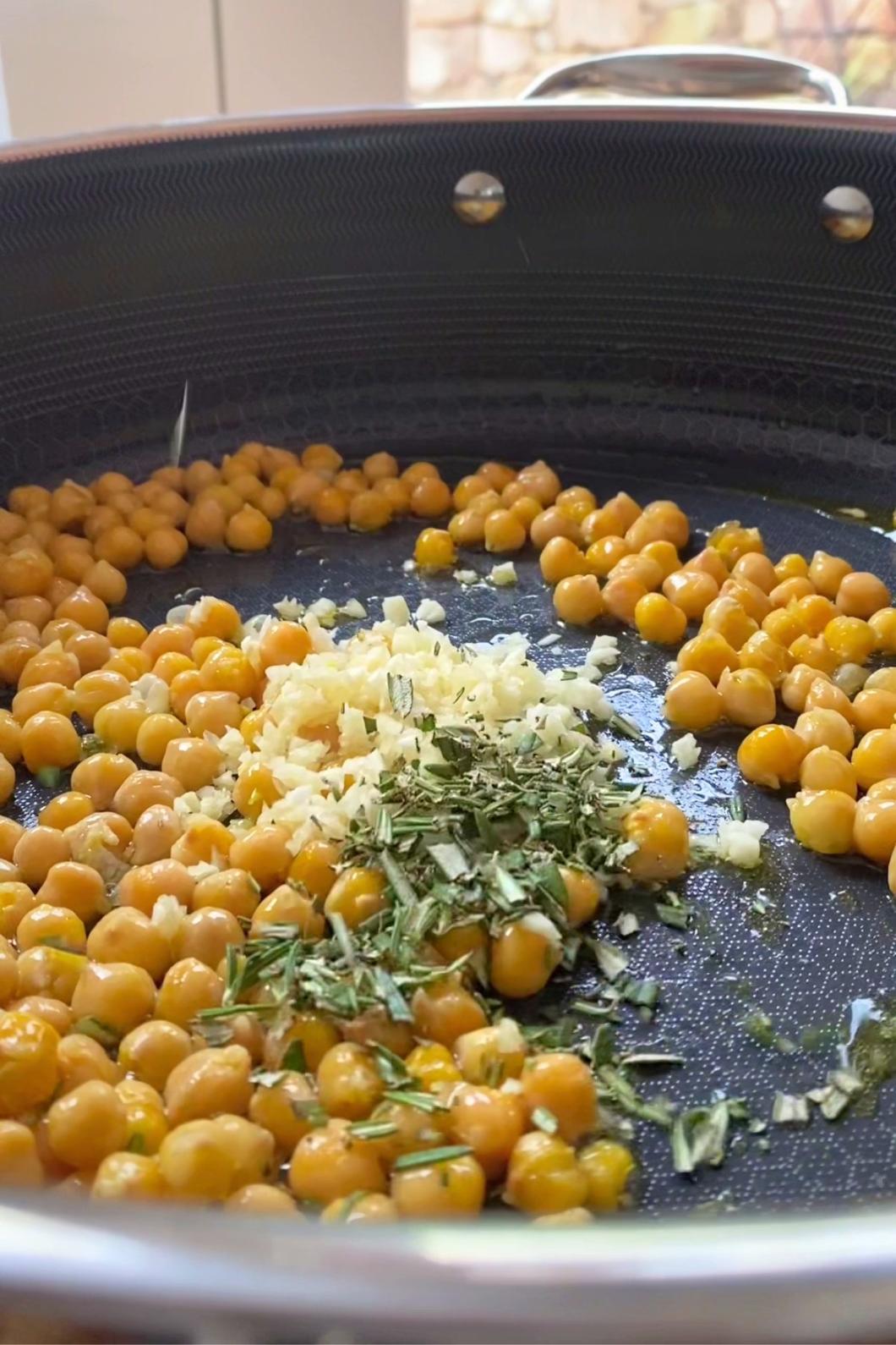 Chickpeas, chopped garlic, and herbs sizzling in a non-stick skillet.