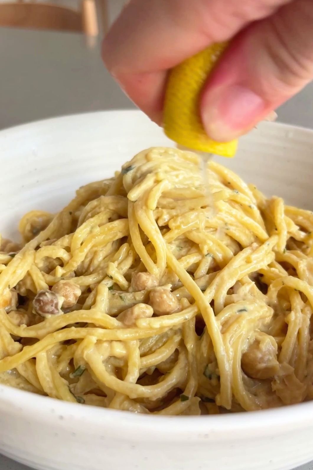 A hand squeezes lemon juice over a bowl of creamy spaghetti with chickpeas.