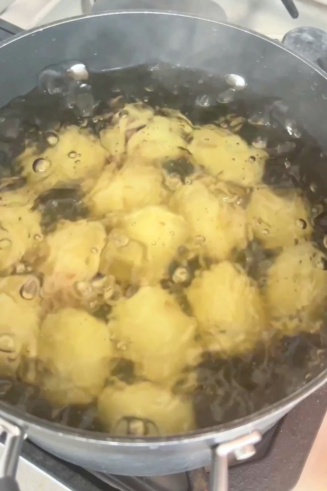 Potatoes boiling in a large pot of bubbling water on the stove.