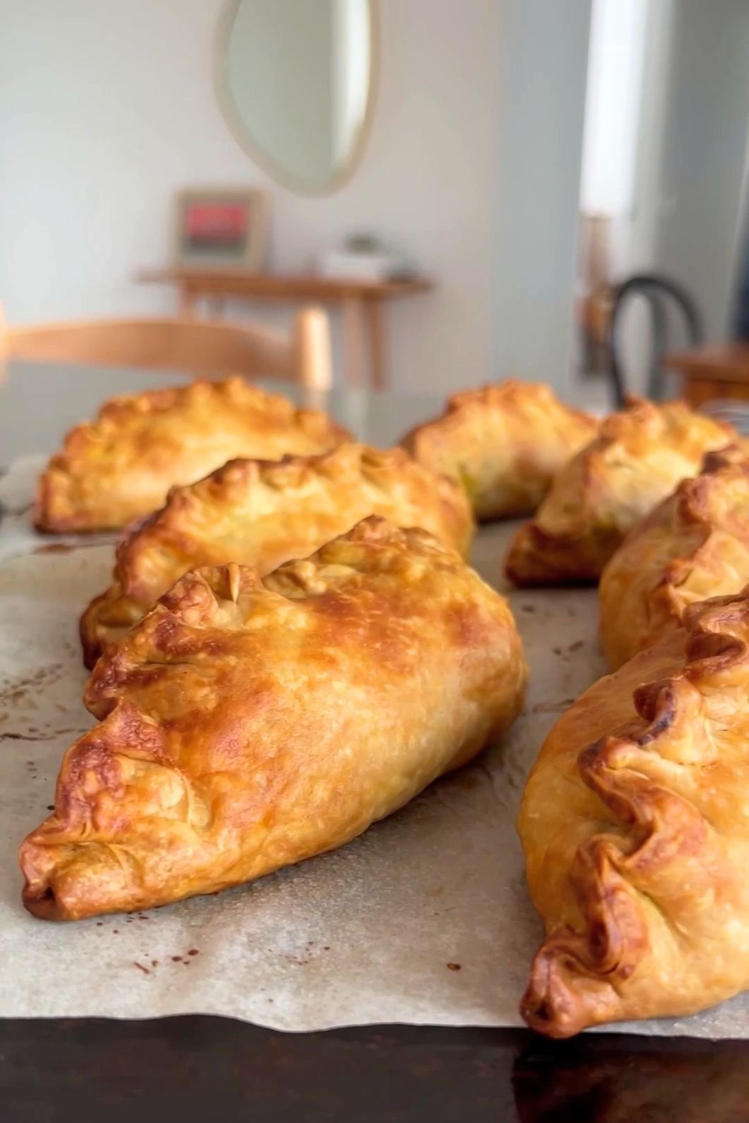 Golden-brown baked pasties sit on parchment paper, fresh from the oven.