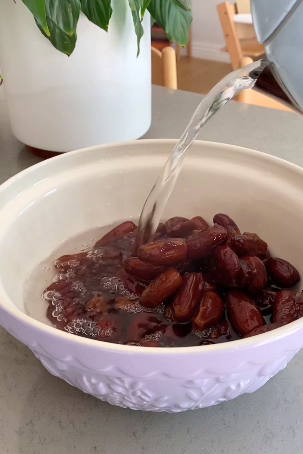Hot water being poured over dried dates in a white bowl to soak and soften them.