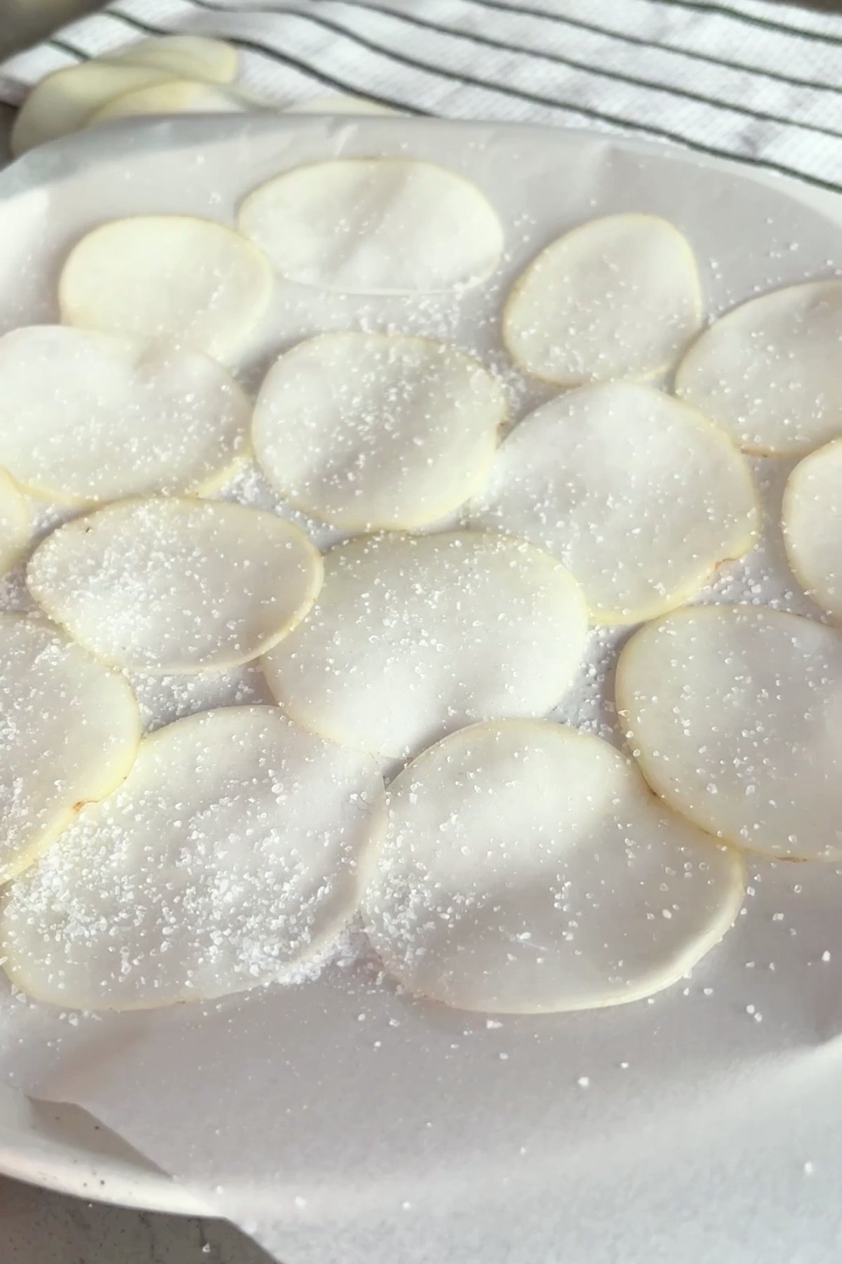 Thin potato slices arranged on parchment paper, sprinkled evenly with coarse salt.