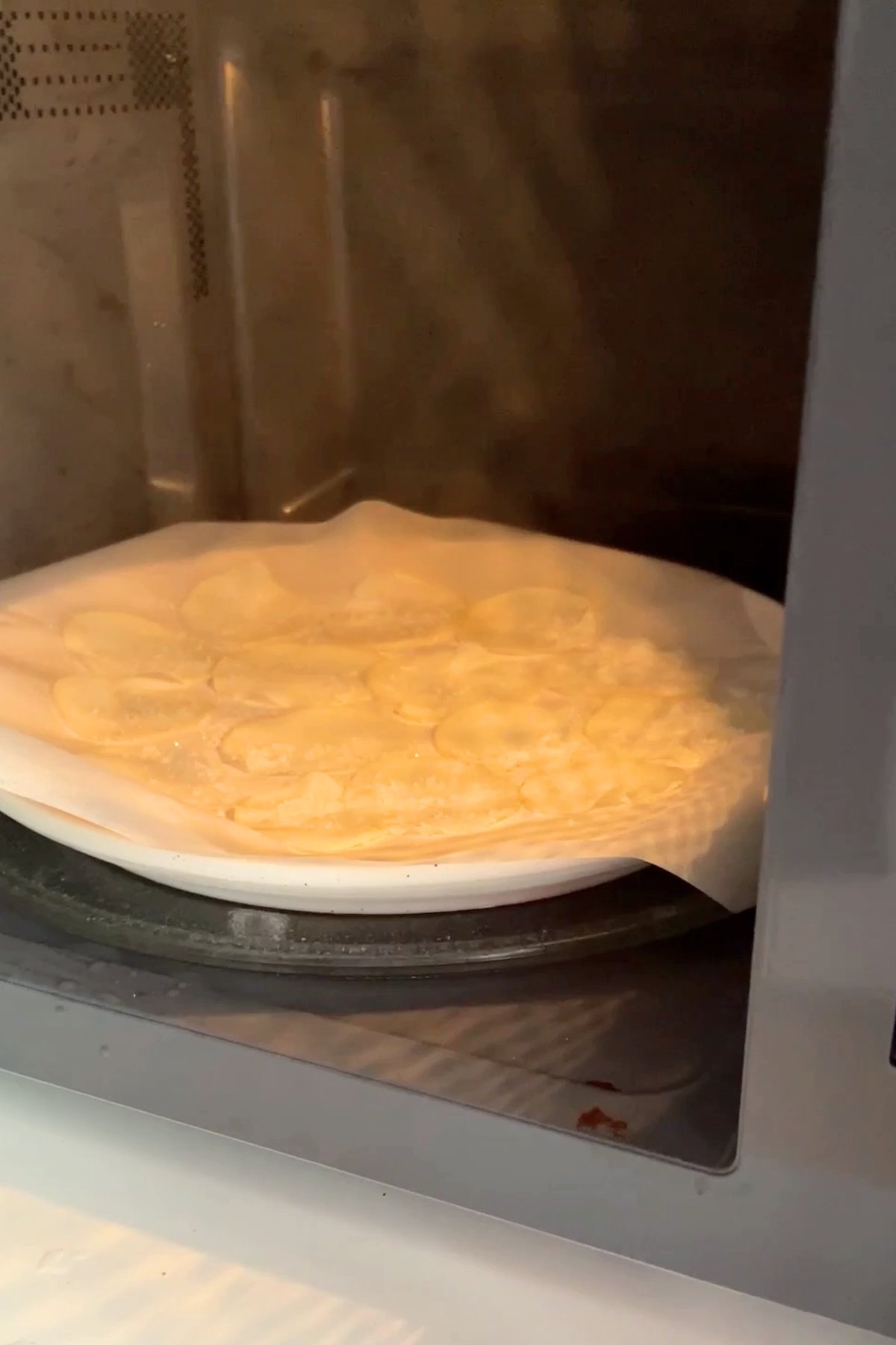 Thin potato slices on parchment paper inside a microwave.