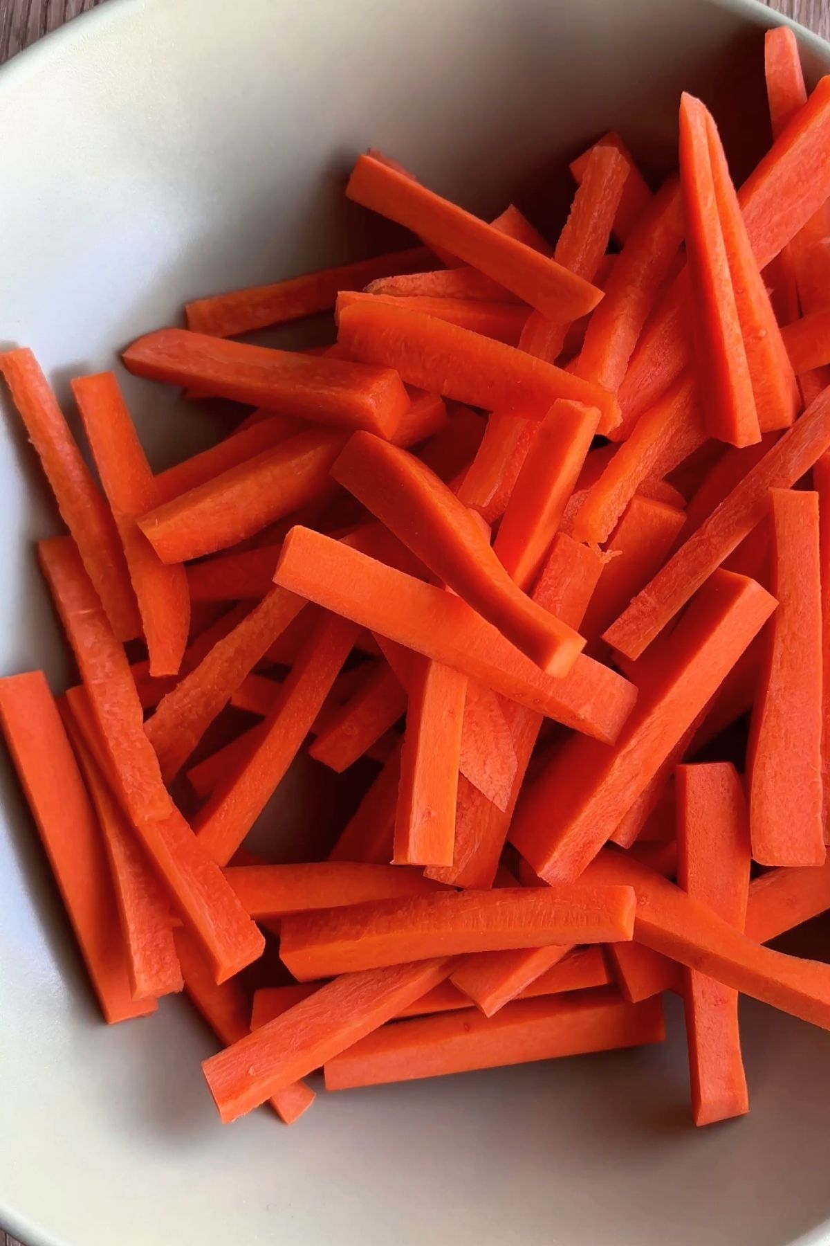 A beige bowl filled with vibrant, julienned orange carrot sticks.