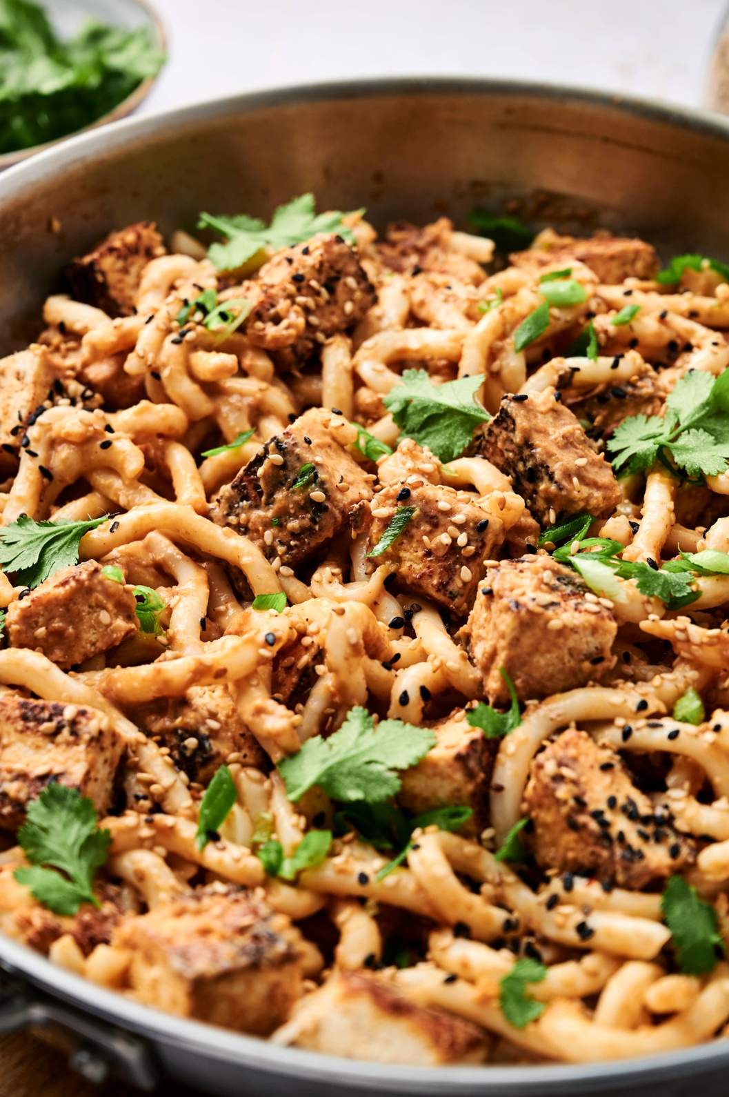 Pan of noodles and cubes sprinkled with seeds and chopped green.