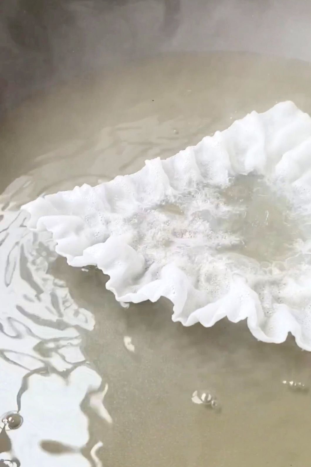 Puffed rice paper sizzling in a shallow layer of oil in a pan.