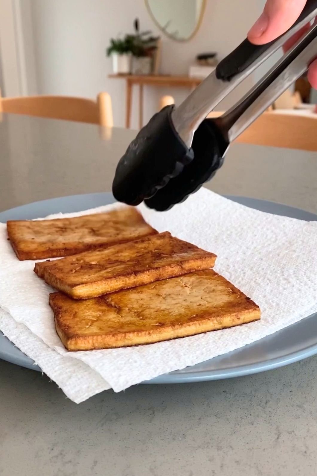 Golden-brown tofu resting on a paper towel–lined blue plate.