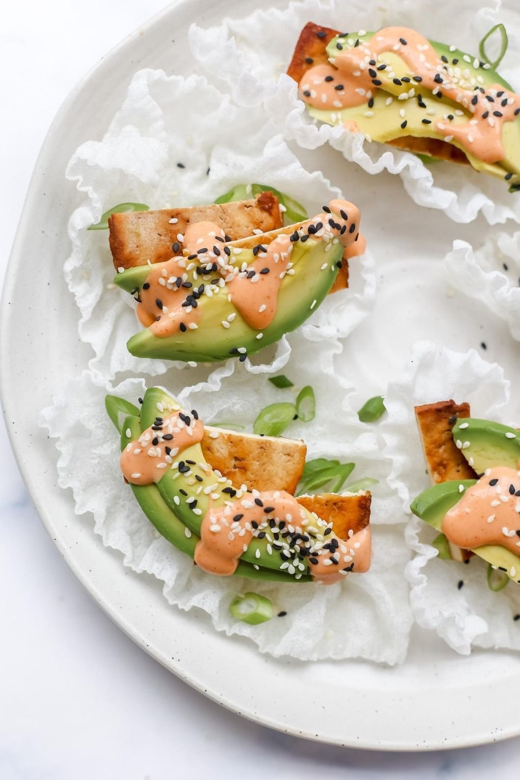 Crispy rice paper topped with avocado slices, grilled tofu, orange sauce and black and white sesame seeds.