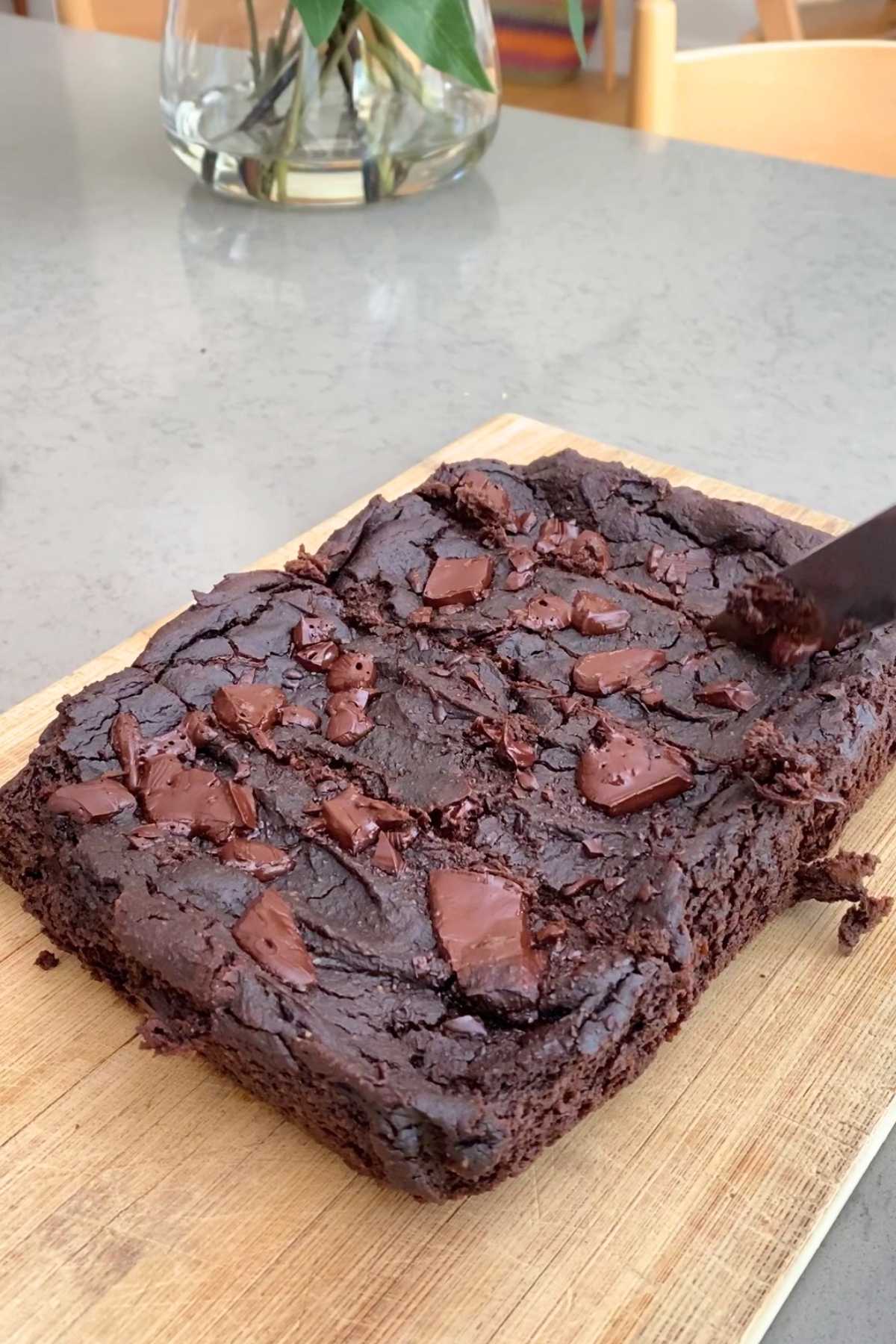 A rich, chocolate brownie with chunks of chocolate on a wooden board.
