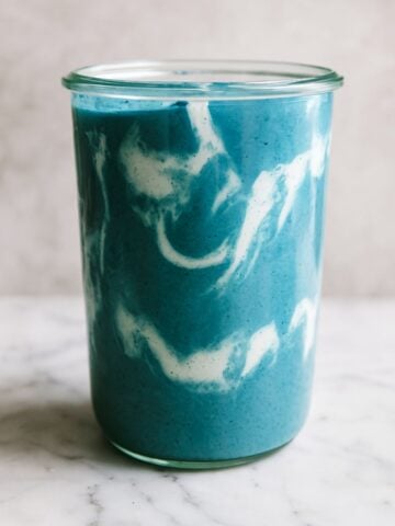 Swirled blue and white smoothie in a clear glass jar on a marble surface.