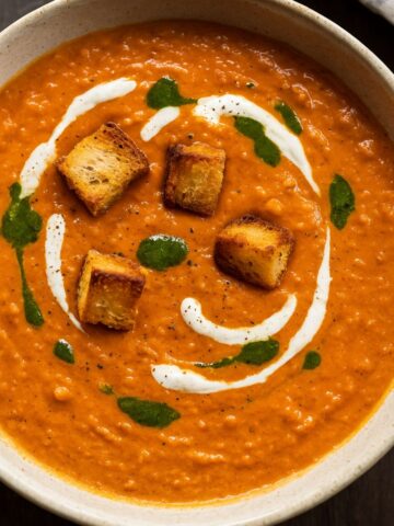 Cherry tomato soup with golden croutons, swirled yogurt, and green herb oil on top.