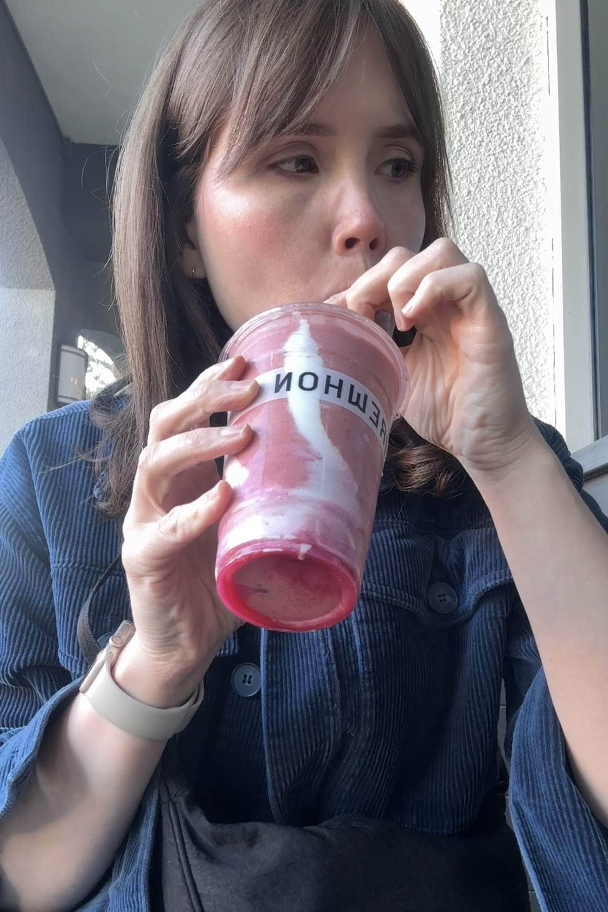 Sipping a pink smoothie with a white swirl from an Erewhon cup.