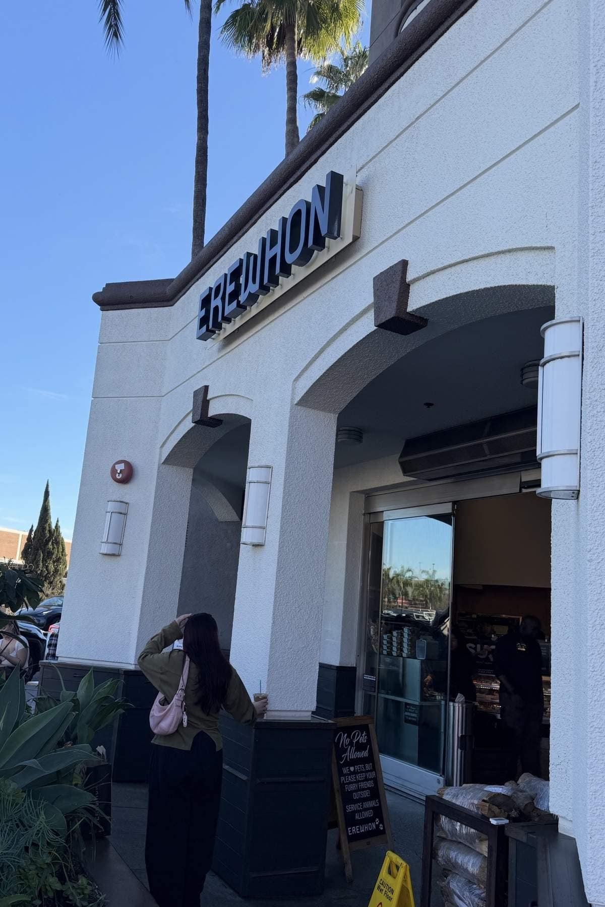 Erewhon storefront with palm trees against a clear blue sky.
