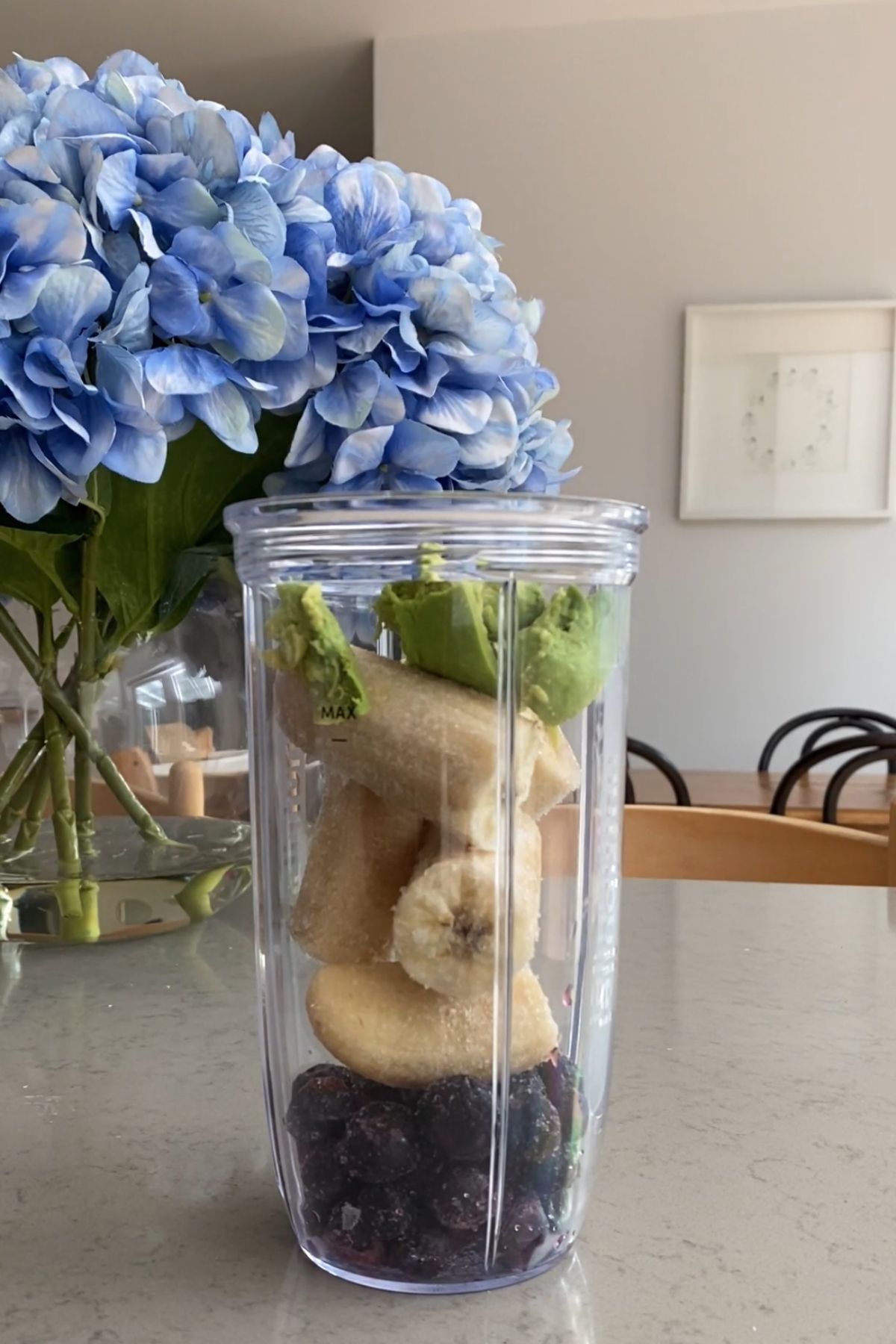 Frozen blueberries, banana pieces, and avocado chunks layered in a clear blender cup on a kitchen counter.
