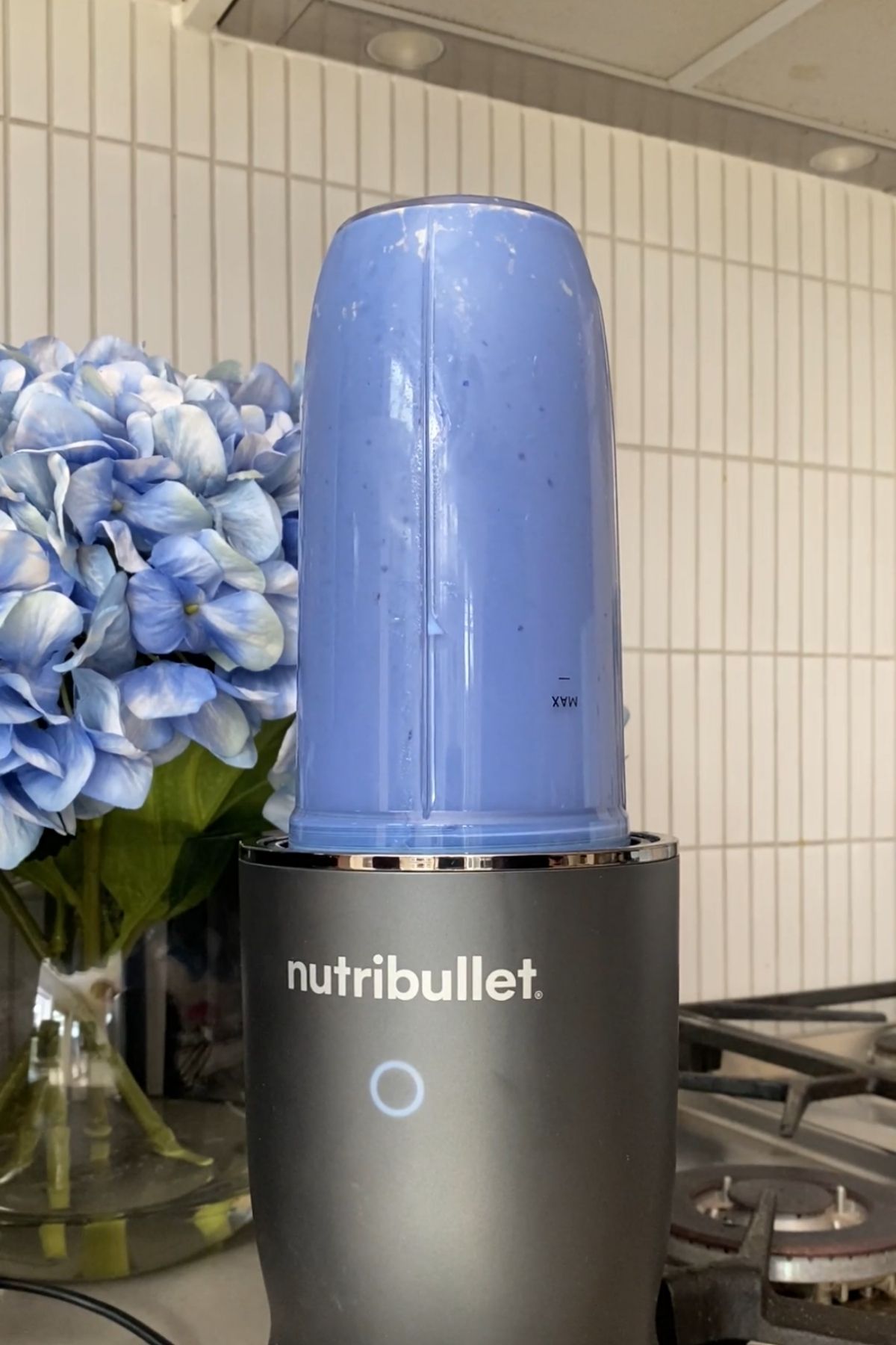 Blue smoothie blending in an upside-down Nutribullet blender on a kitchen counter near a vase of hydrangeas.