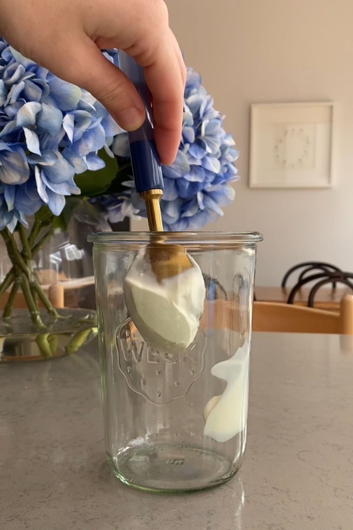 Clear Weck jar with white yogurt smears around the inside, sitting on a kitchen counter near a vase of blue hydrangeas.