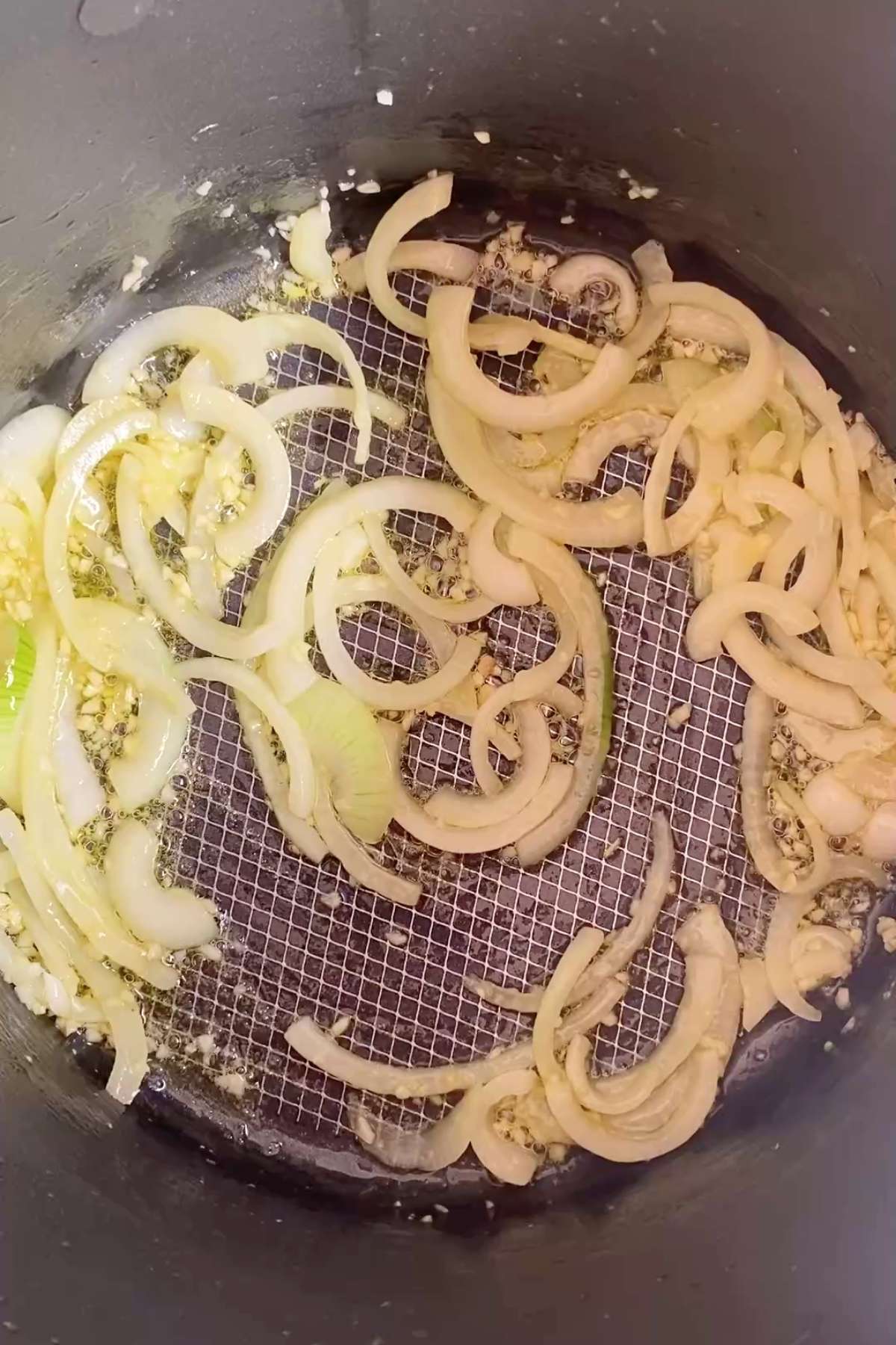 Sliced onions and minced garlic sizzling in oil at the base of a large pot.