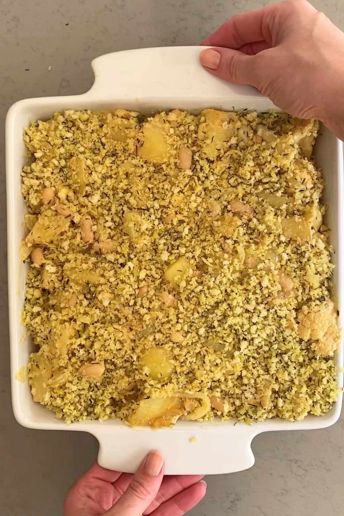 Unbaked gratin topped with a golden, herbed breadcrumb mixture in a white square baking dish, ready for the oven.