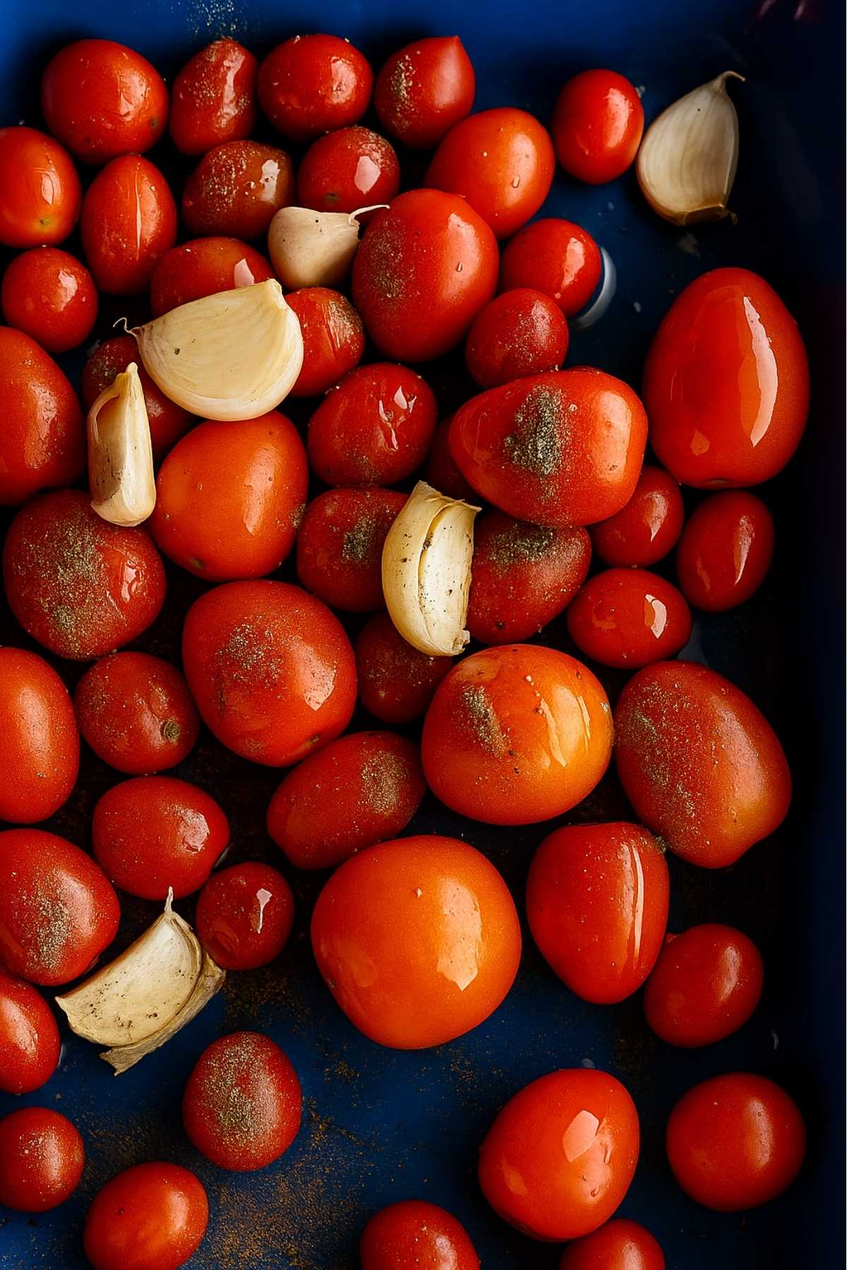 Cherry tomatoes and garlic cloves sprinkled with pepper and olive oil in a tray.