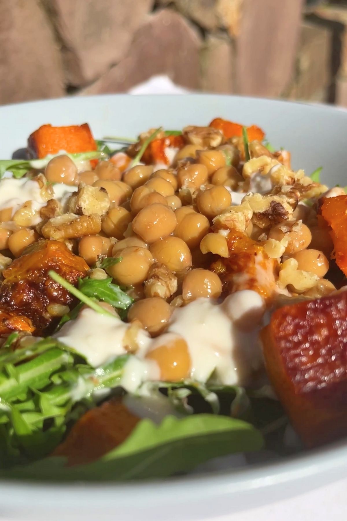 Close-up of chickpeas, roasted pumpkin, and walnuts topped with creamy dressing on a bed of fresh arugula.