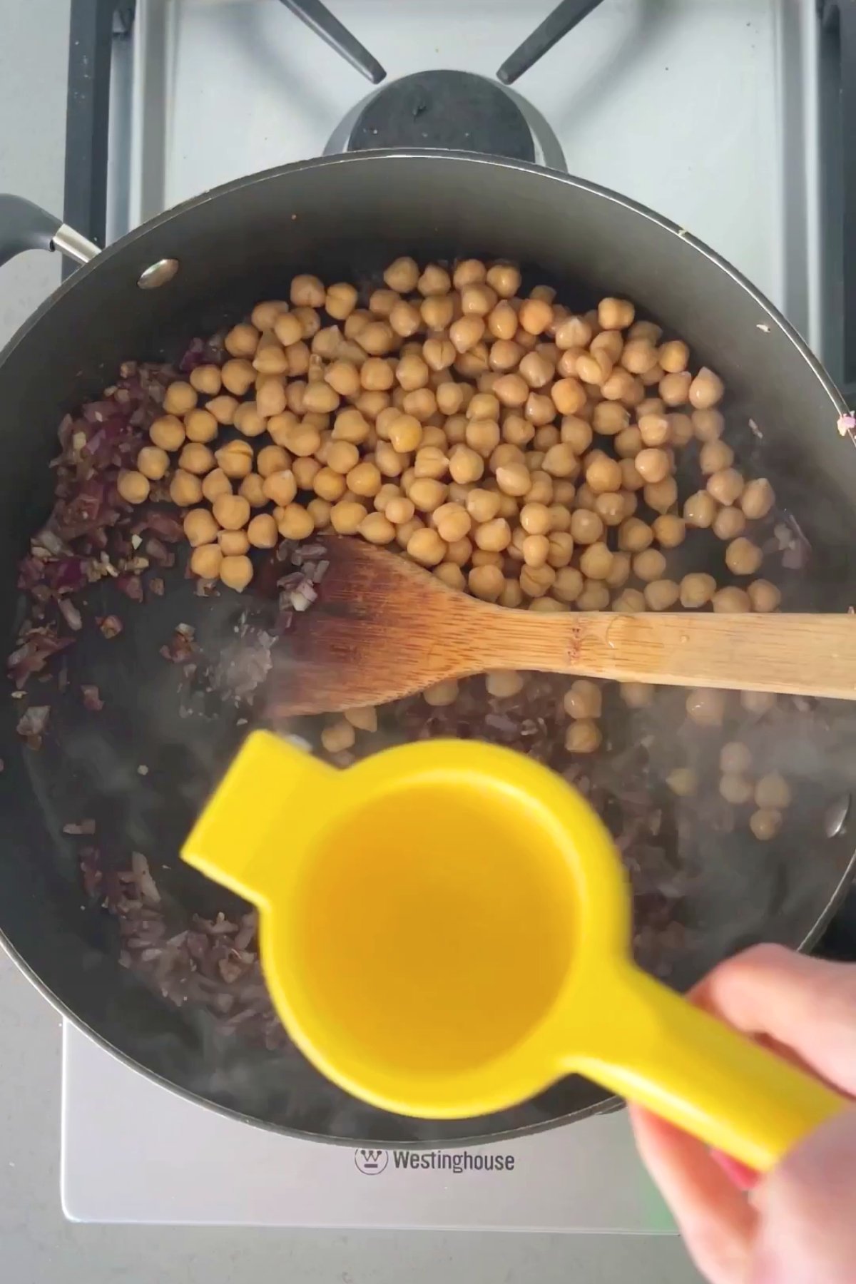 Chickpeas added to sautéed onion and spices as lemon juice is squeezed from a yellow citrus juicer.