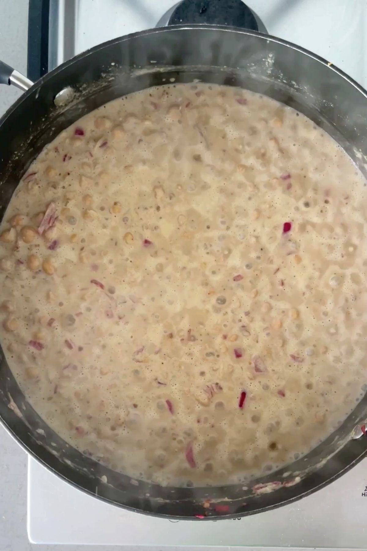 Chickpeas simmering in a creamy sauce with visible red onion pieces in a large black pan.