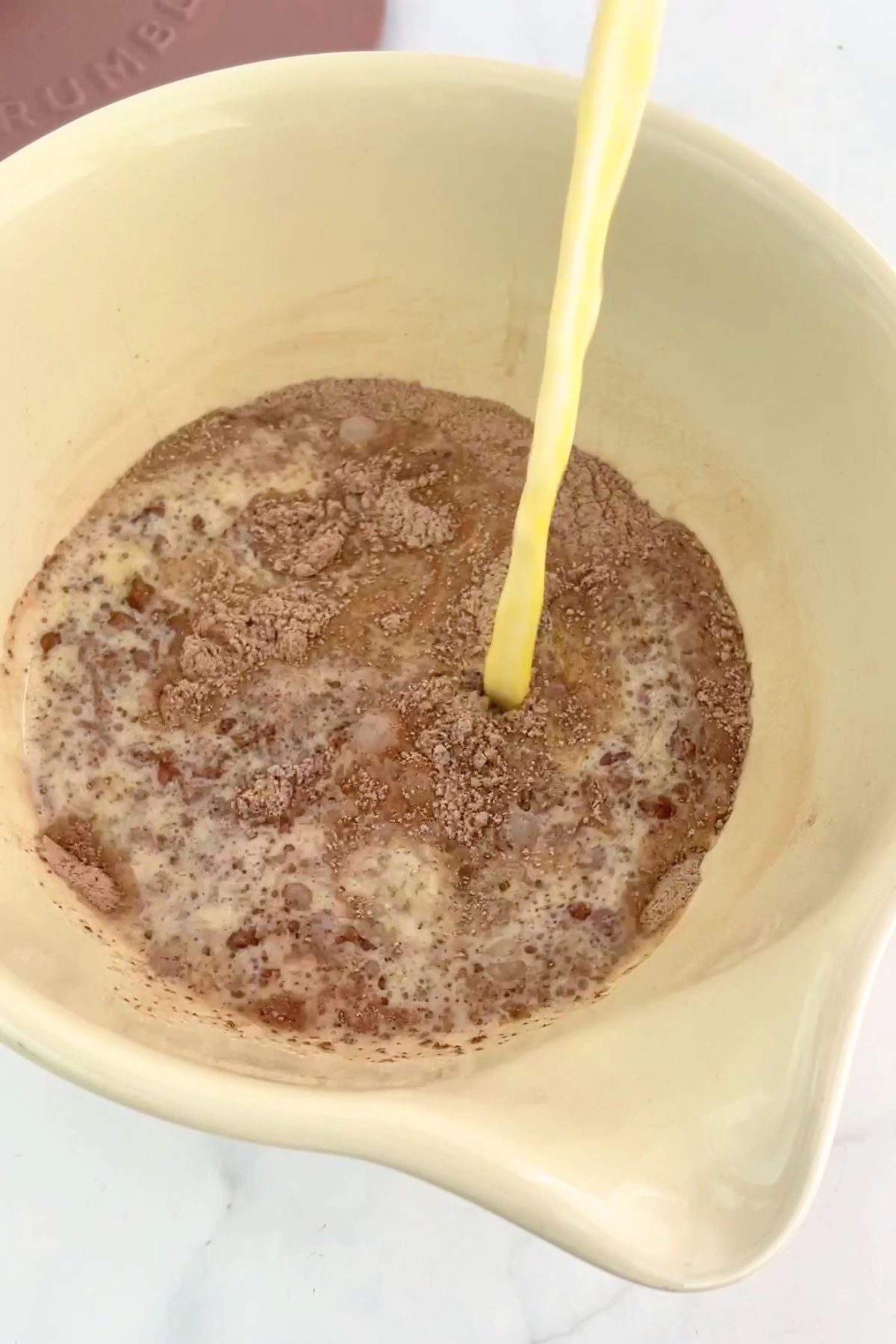 Yellow liquid streams into a bowl of dry cocoa-speckled mix.