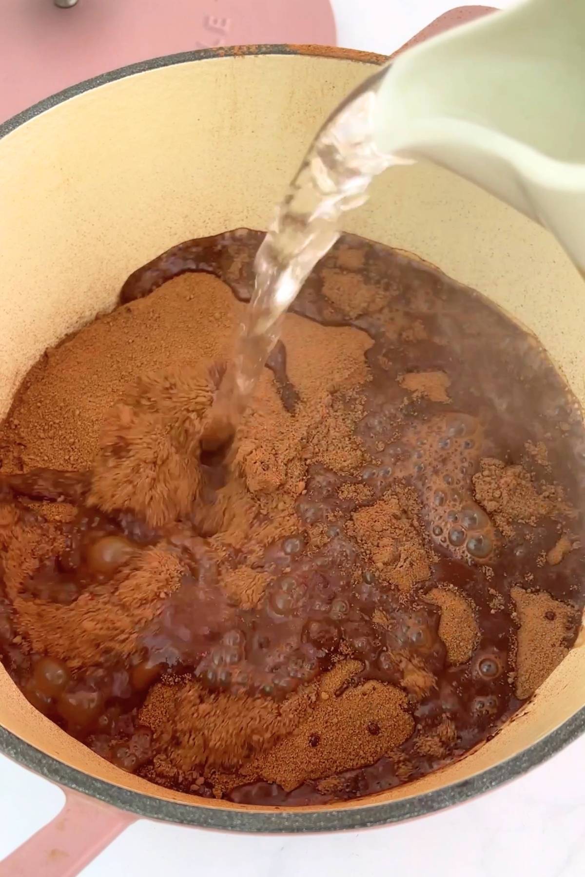 Boiling water pouring from a jug over the cocoa-sugar layer in the baking dish.