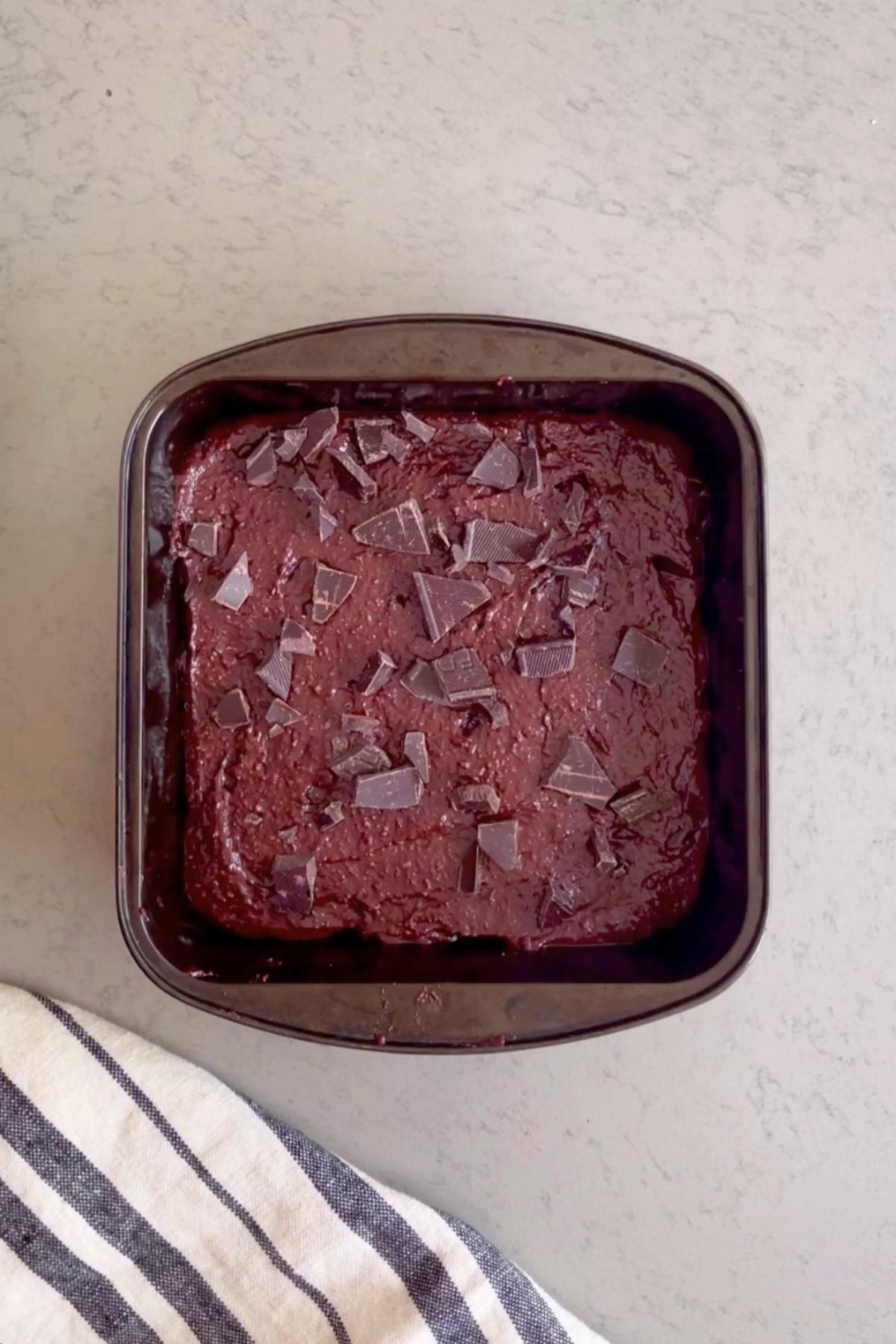 Square pan filled with brownie batter, sprinkled with chopped chocolate pieces.