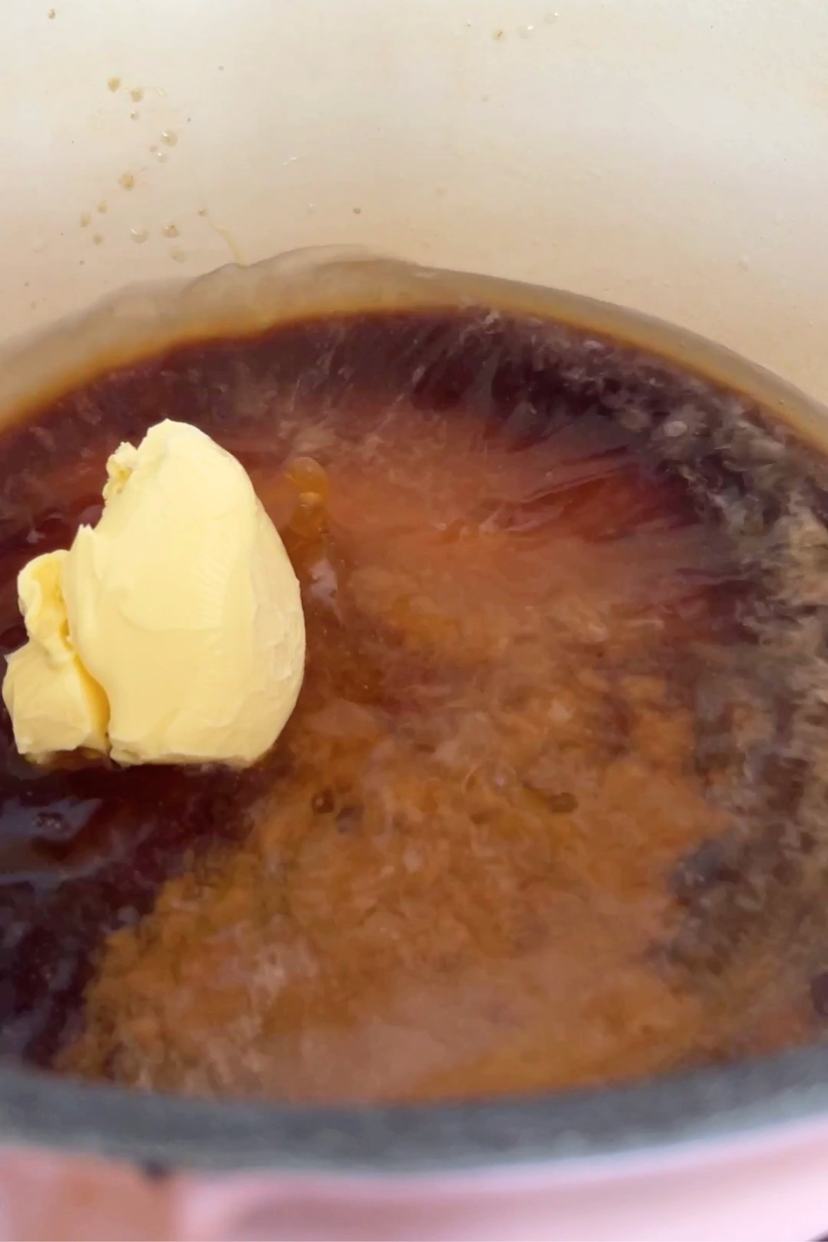 A scoop of margarine begins to melt into a pot of bubbling golden brown syrup.