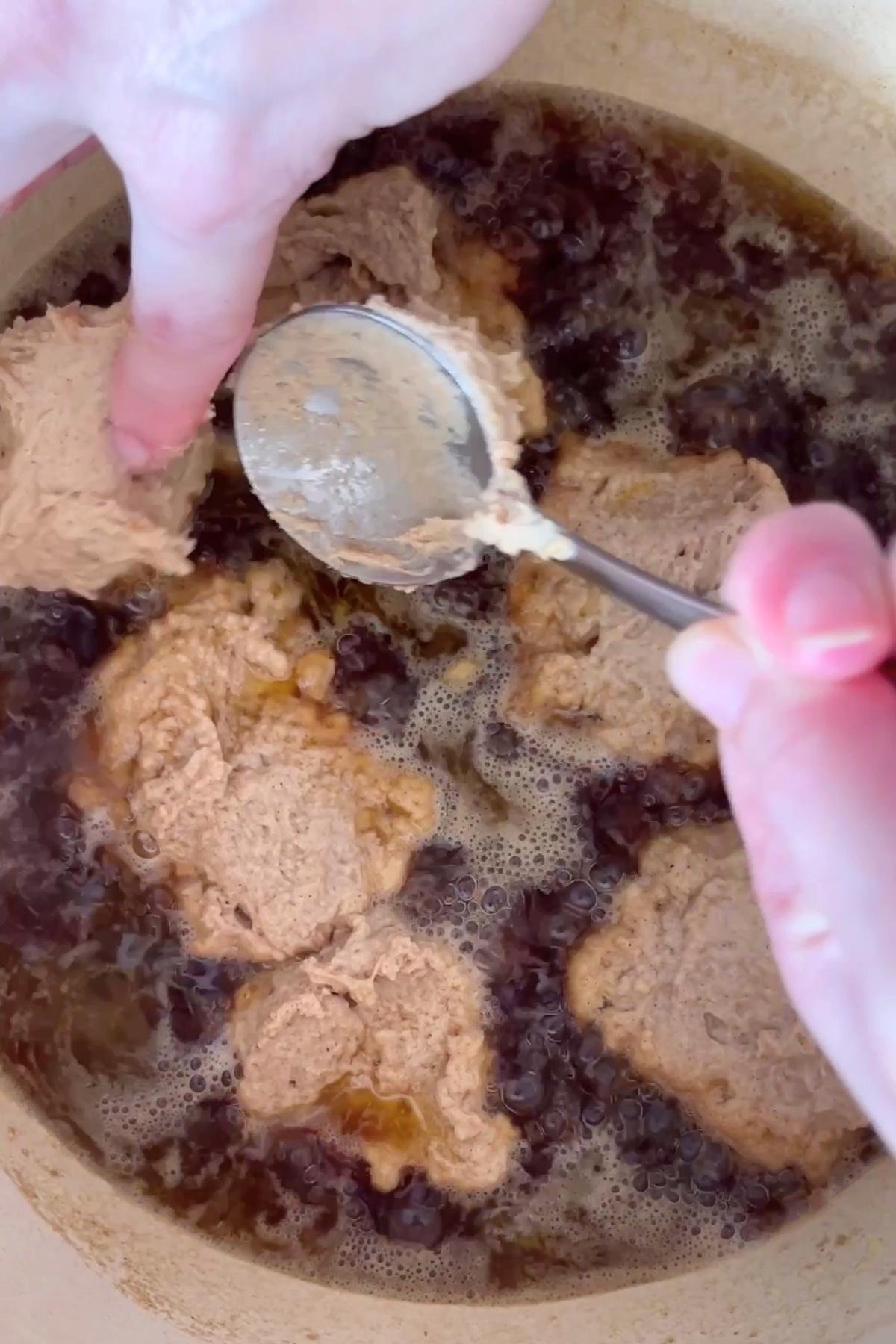 Sticky spoonfuls of dumpling batter being dropped into simmering syrup in a pot.